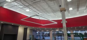 Electrical installation of a suspended rectangular LED light fixture at The Edge Fitness Clubs, showing conduit, ceiling wiring, and the illuminated accent lighting along the curved red wall during construction.
