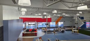 Wide overhead view inside The Edge Fitness Clubs showing ongoing electrical installation, including high-bay LED lighting, conduit runs, and power distribution work across the open gym floor. Tools, materials, and raised platforms are visible as electricians complete the facility’s lighting and power systems.