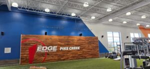Electrical installations completed at The Edge Fitness Clubs in Pike Creek, featuring overhead lighting, suspended track lights, and ceiling-mounted electrical systems above the turf training area.
