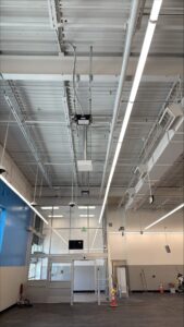 Interior of a retail space showing overhead conduit, cable trays, suspended wiring, long LED strip lighting, and HVAC ductwork above the entrance area during an electrical installation.