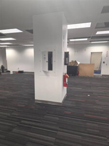 Office renovation space with electrical panels mounted on a central structural column, surrounded by partially completed ceiling work and construction materials.