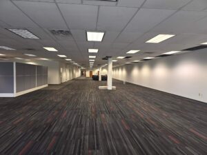 Large open office space with completed grid lighting, finished carpeting, and newly installed wall outlets, showing the final stage of a commercial electrical fit-out.